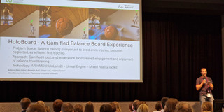 This image shows Robin Frölke standing on a large stage in front of the conference audience. In the background, we see a slide that showcases the work he presented, HoloBoard.